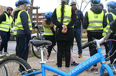 Groupe de personnes avec des gilets jaune devant un vélo bleu