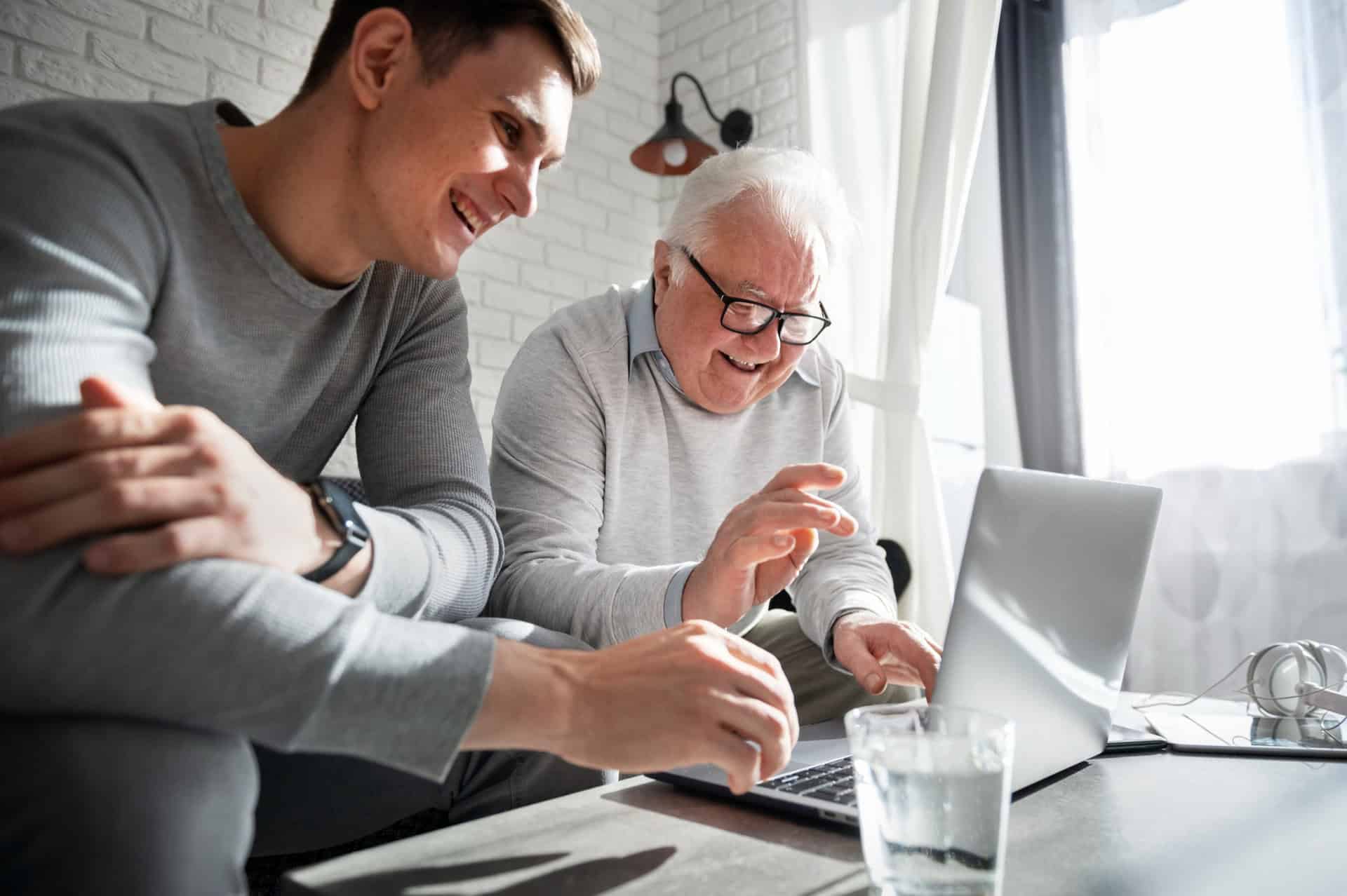 grand-père apprenant à utiliser un ordinateur avec un jeune homme